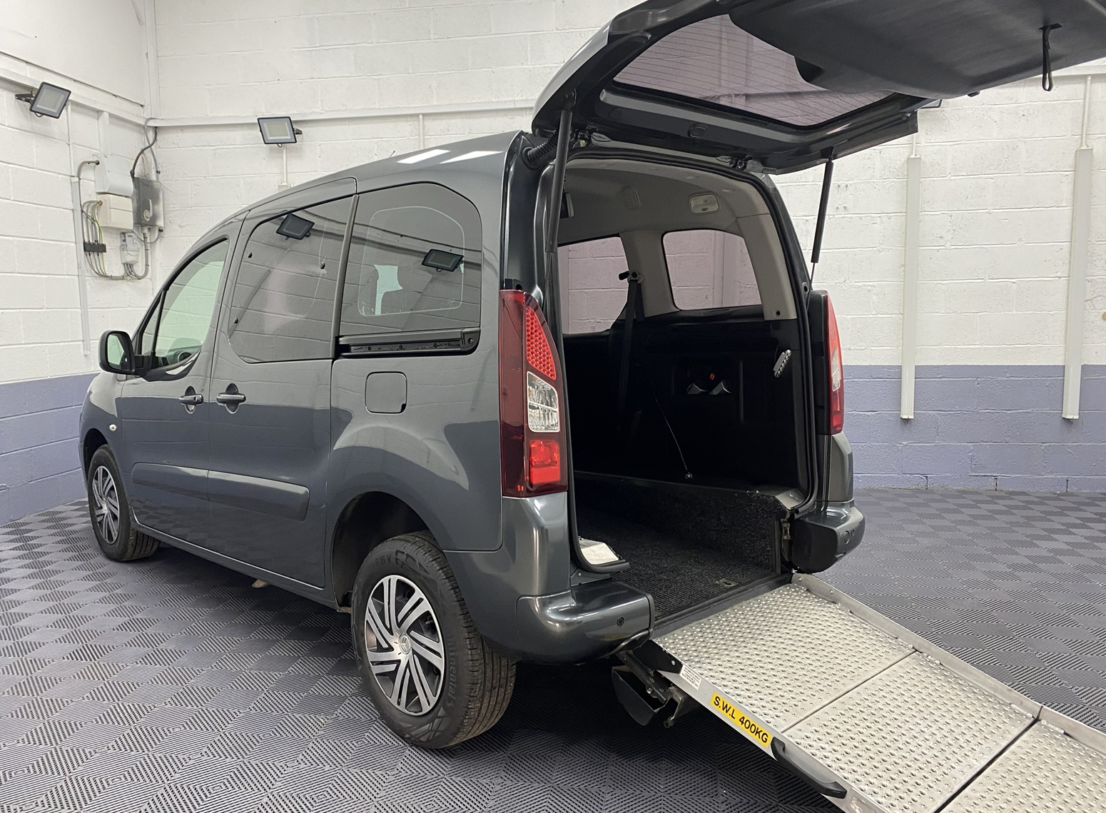 A Grey wheelchair accessible accessible (WAV) Citroen Berlingo Rear side view with boot open and rear ramp folded out NK68 AYF 9