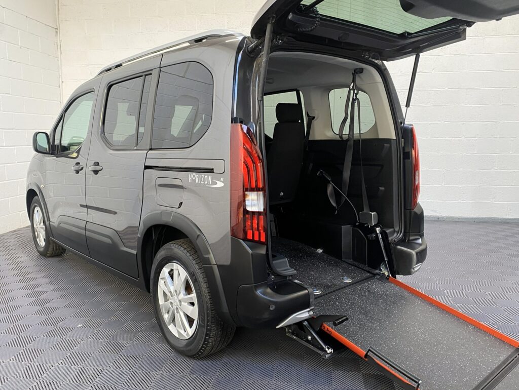 Rear view of Peugeot Rifter WAV wheelchair accessible vehicle for sale at Michael Harraway Cars, Weston-super-Mare, showing lightweight fold-flat rear ramp deployed and interior space for one wheelchair user with three passenger seats. Sf20 GNP 1