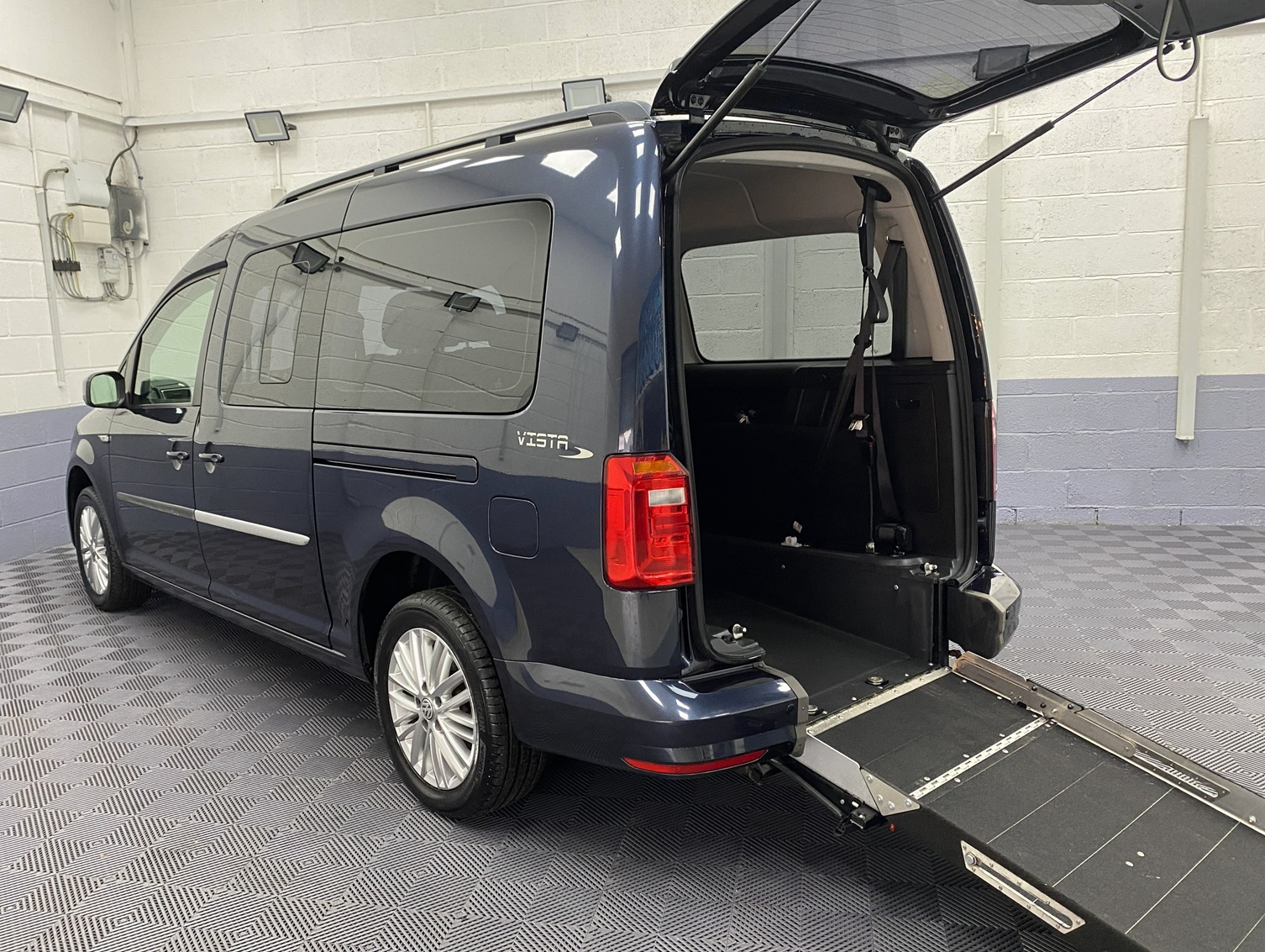 A blue Volkswagen Caddy Maxi Petrol wheelchair accessible vehicle rear view showing ramp folded down. YY68 LHYF